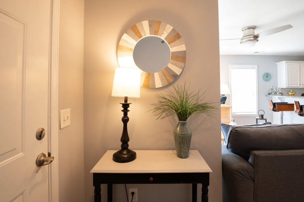 A warm and inviting entryway featuring a console table adorned with a potted plant and decorative lamp, set against a mirrored wall that reflects soft lighting. The setting evokes the feeling of arriving at a cozy retreat, with elements that suggest a welcoming atmosphere for couples.