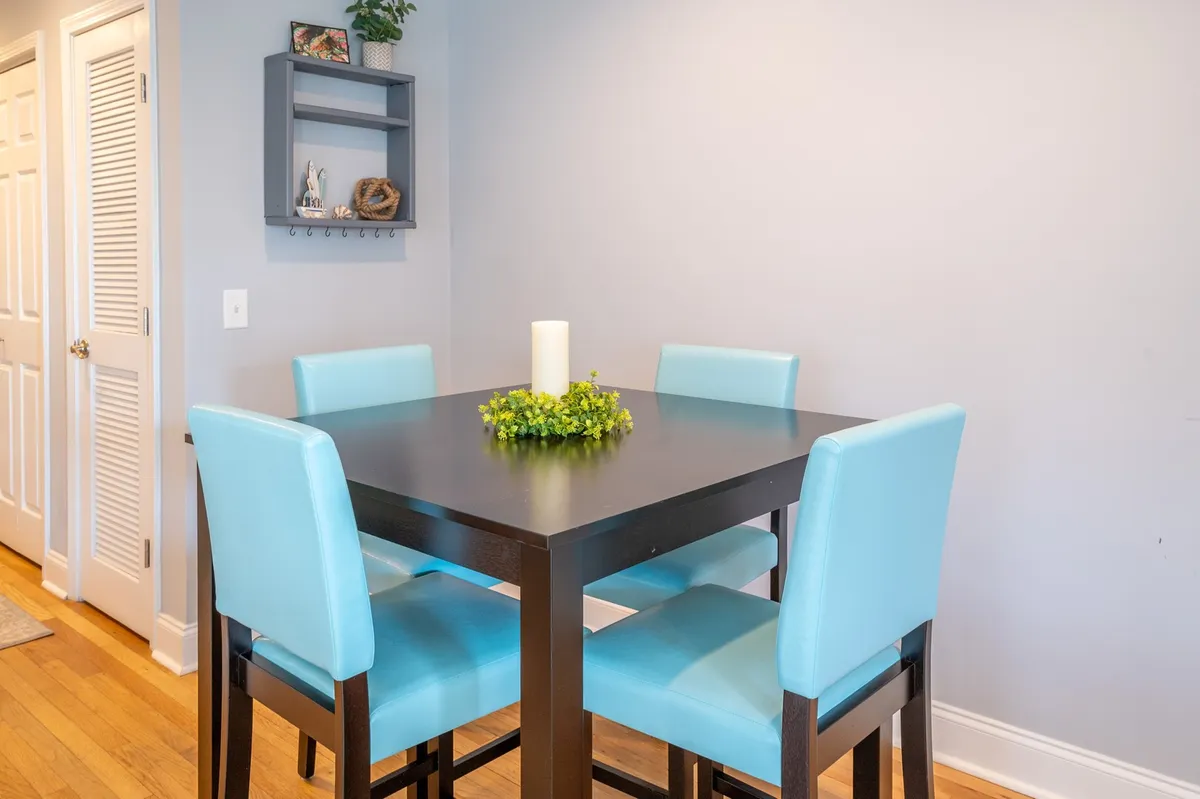A cheerful dining space featuring a black dining table surrounded by turquoise chairs, a green centerpiece, and tastefully arranged decor on a wall shelf. The setup is perfect for casual meals and intimate conversations with friends after exploring local dining and nightlife.