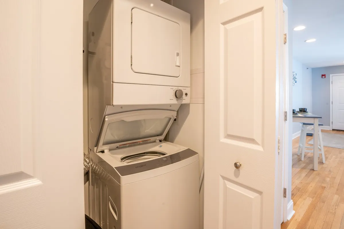 A close-up of a stackable washer and dryer unit neatly tucked behind white closet doors. The setup is modern, compact, and emphasizes in-unit convenience.