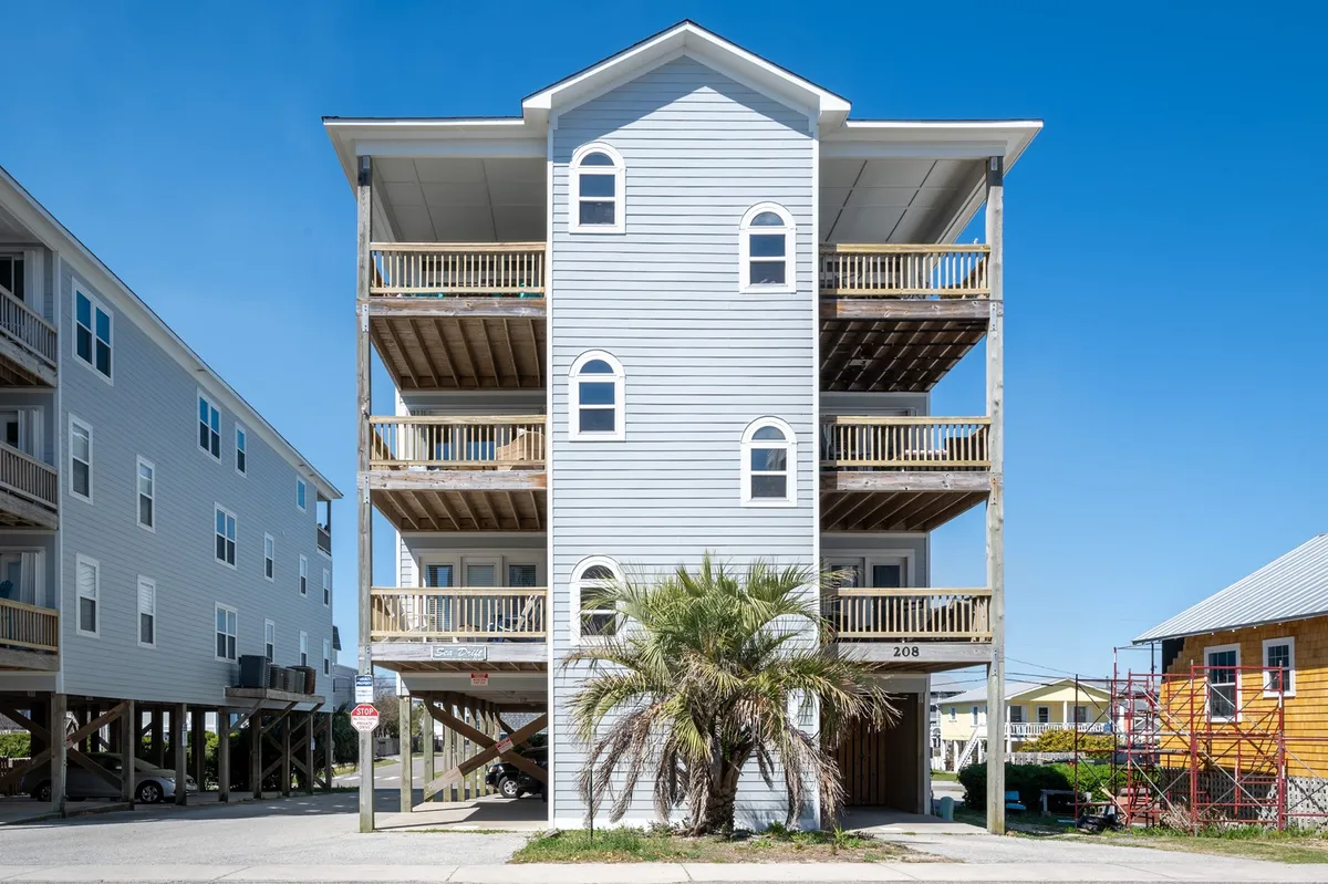 A three-story building with a bright blue exterior stands out, complemented by balconies with wooden railings and a palm tree in the foreground. The scene is cheerful and relaxed, suggesting guests can enjoy the beach nearby and socialize with family and friends on the balconies. The image hints at a vibrant local culture and the enjoyment of outdoor spaces.