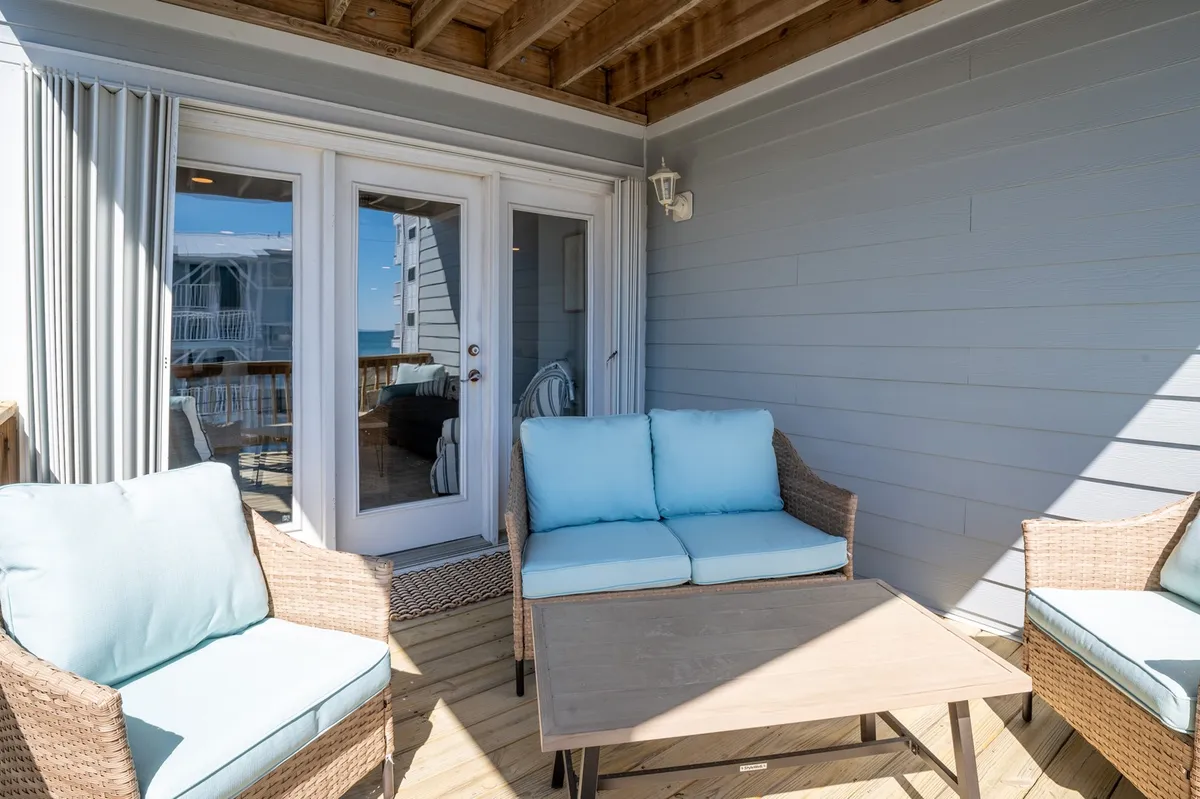 An inviting balcony with outdoor seating, sliding glass doors, and a stunning beach view beyond. The mood is serene, perfect for unwinding as the sun sets over the ocean.