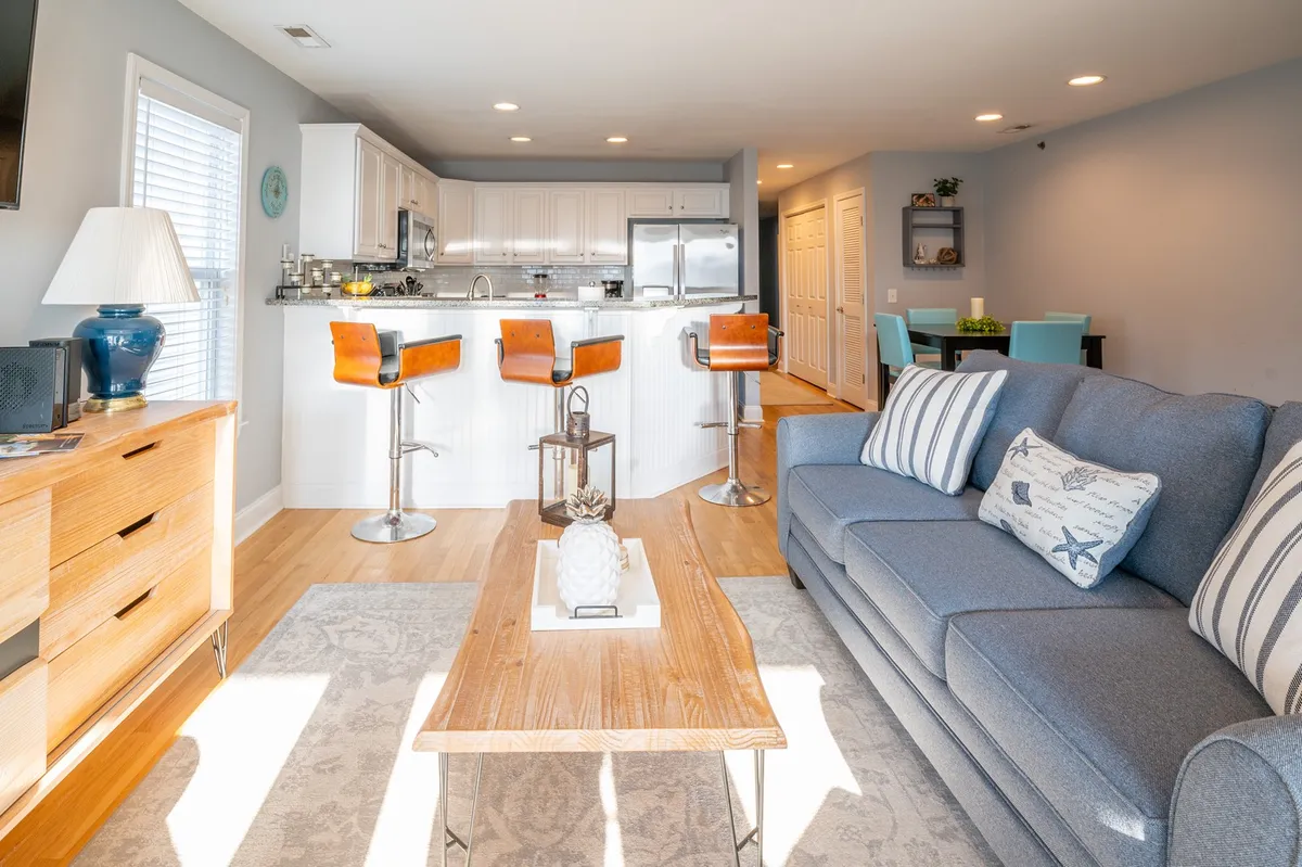 This image showcases a comfortable living area with a sofa, kitchen island, and bar stools, set up for socializing, cooking, and relaxing. The open layout suggests a great spot for entertaining or winding down after a busy day out, with plenty of natural light and inviting decor.