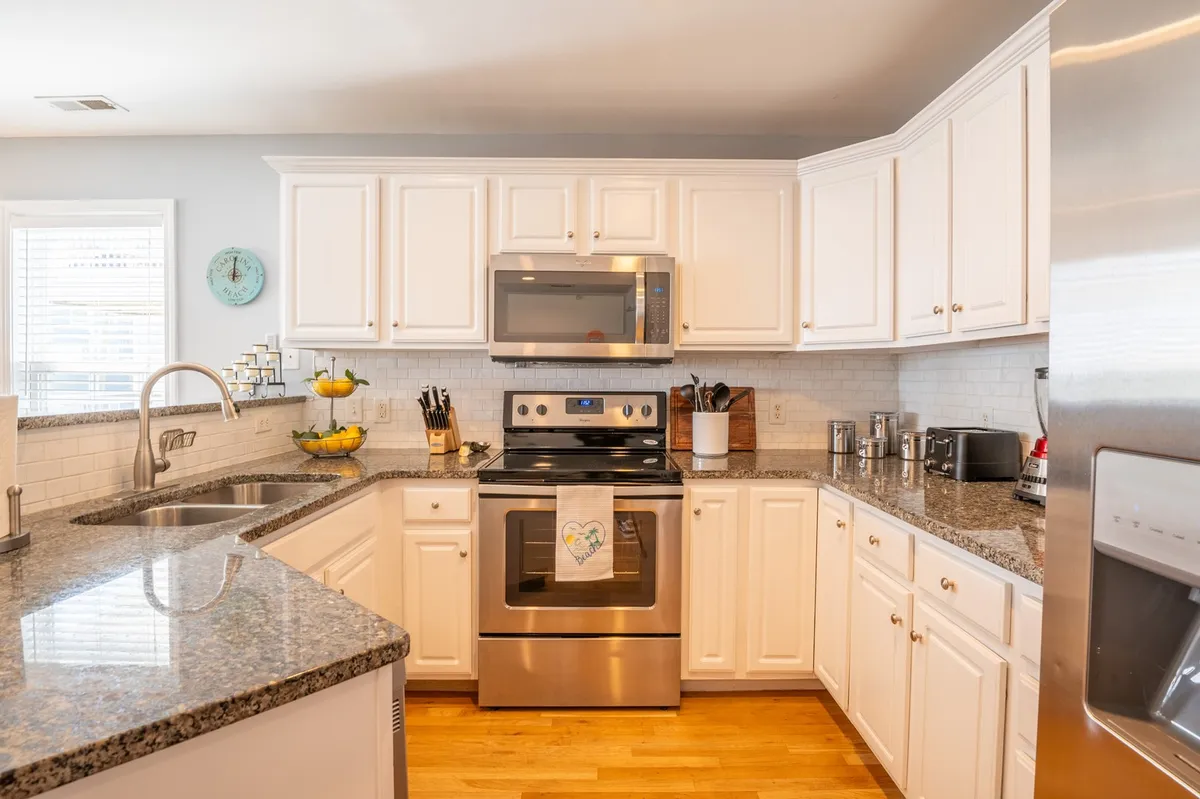 A bright, homey kitchen space featuring a granite countertop, stainless steel appliances, white cabinetry, and a window letting in ample natural light. The setup is ideal for family gatherings and meal preparation, reinforcing a sense of togetherness.