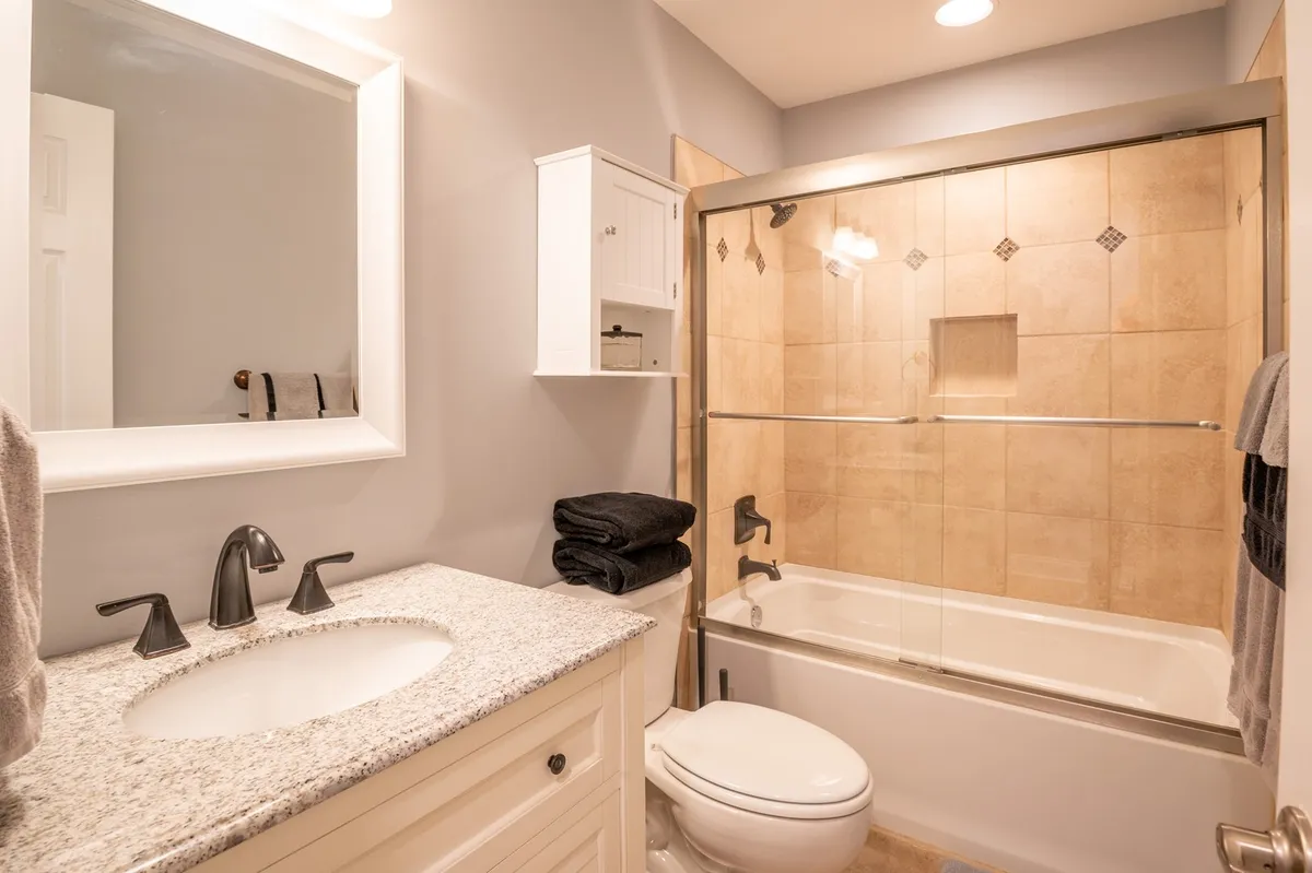 A modern bathroom with a granite countertop, glass shower door, and soothing colors. The space feels inviting, perfect for unwinding with a refreshing shower or calming evening routine.