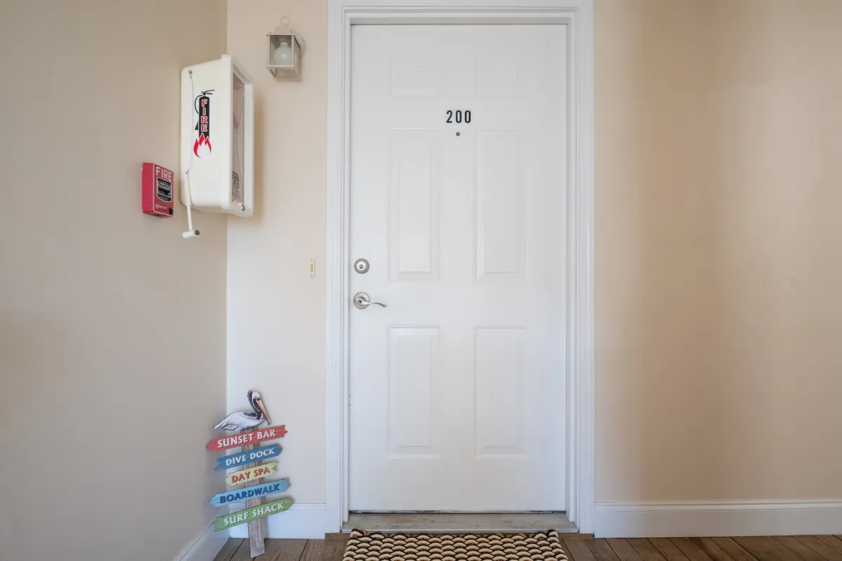 This image captures the private entrance to unit 200, featuring a door with a prominent number, a colorful signpost directing to nearby attractions, and a welcoming mat. The scene feels inviting and gives a first impression of exclusivity and warmth.